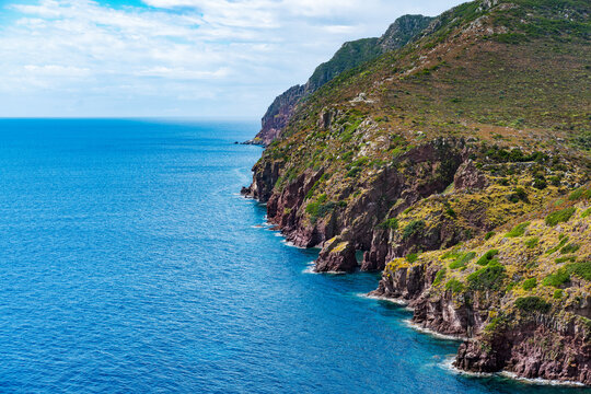 Breathtaking cliffs and rugged coastline of Capraia Island, Italy, meeting vibrant turquoise Mediterranean waters under a cloudy sky, revealing nature's raw beauty