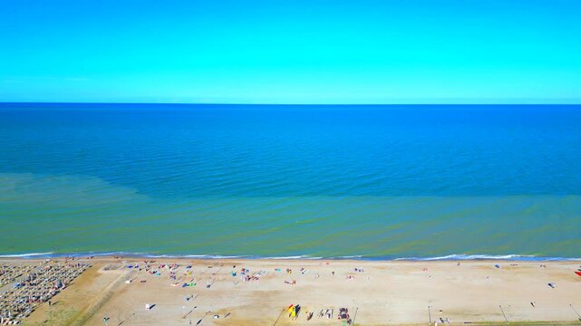 Splendid aerial truck right shot of the Adriatic Sea in Marina Palmense, sandy beach, vast expanses of clean azure and aquamarine waters reaching the clear horizon, atmosphere imbued in balmy sunlight