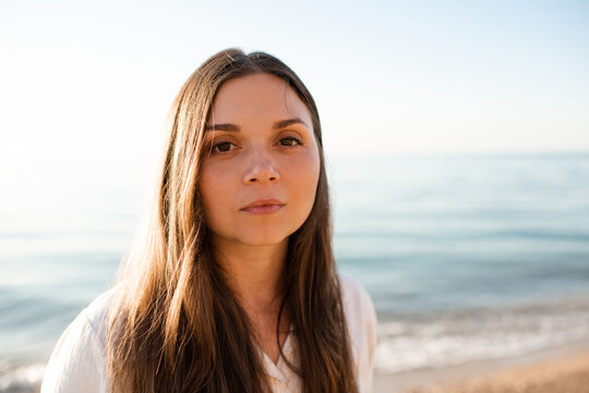 Portrait of young adult woman with naked healthy skin without make up over sea background. Looking at camera.