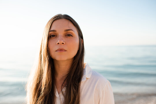 Portrait of young adult woman with naked healthy skin without make up over sea background. Looking at camera.