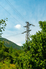 Fototapeta premium High-voltage transmission tower surrounded by forested mountains in northern Italy