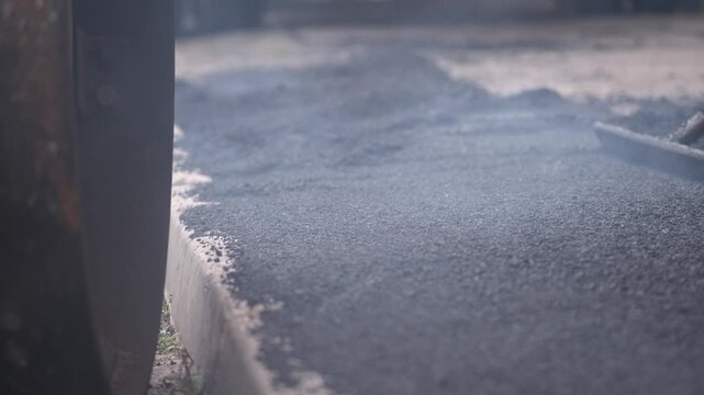 A closeup shot of a construction rake leveling steaming hot freshly poured black asphalt during walkway reconstruction.