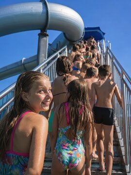 Viele Kinder warten voller Vorfreude auf der Treppe zur gro&szlig;en Wasserrutsche im deutschen Freibad. Die sommerliche Szene zeigt Ferienbetrieb, Spannung und beliebten Badespa&szlig;.
