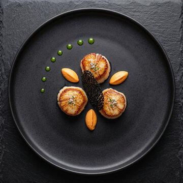 Coquilles Saint-Jacques po&ecirc;l&eacute;es de haute gastronomie sur assiette noire