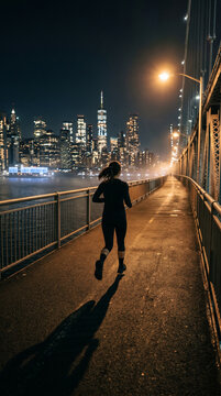 Femme qui court la nuit sur un pont avec la ville illumin&eacute;e en arri&egrave;re-plan
