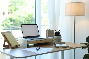 Naklejka premium Workplace with laptop and stationery on table near window in office