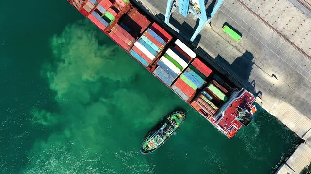 Aerial view of a container ship maneuvering for dock with a tug in the port of Alicante, in the Mediterranean coast of Spain.