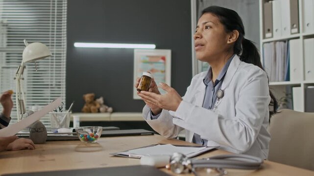 Hispanic female doctor explaining prescription and handing medicine bottle to biracial mother with toddler. Video suitable for pediatric healthcare promotions