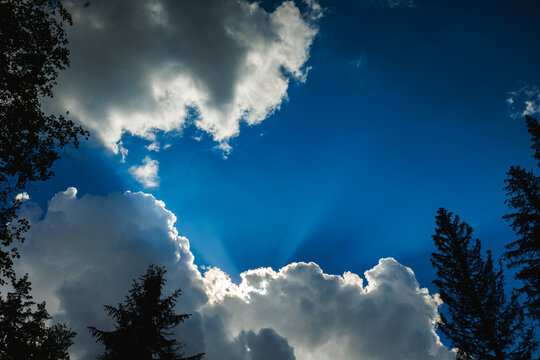 Dramatic blue sky with sun rays shining through fluffy white clouds