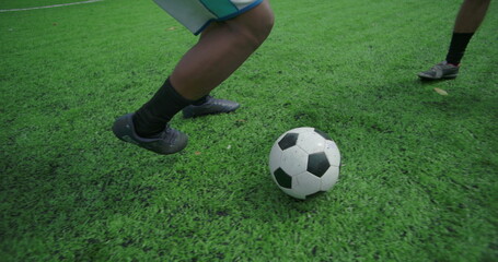 Fototapeta premium Close-up of soccer player running with ball and kicking toward goal during friendly community game, showing movement, coordination, and teamwork on sunny urban field