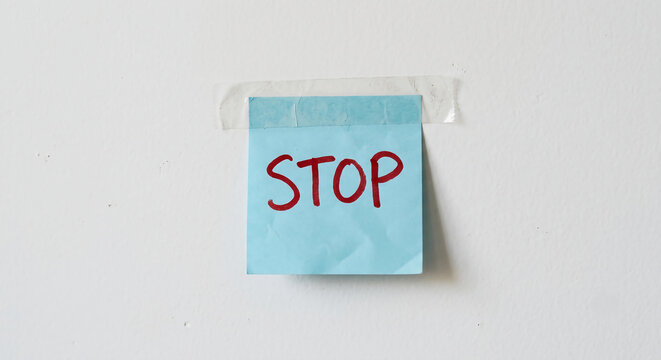 A light blue sticky note with the word "STOP" written in red, taped to a plain white wall.