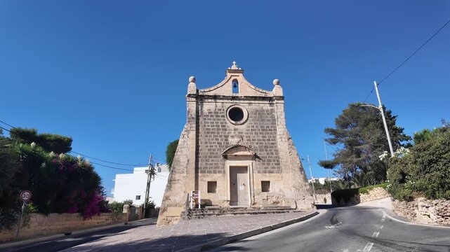 Naxxar, Malta 06.07.2026 - A view of the Chapel of the Annunciation in Salini, Malta, featuring a traditional triangular stone facade, bell tower, and wooden door, standing along a quiet village road 