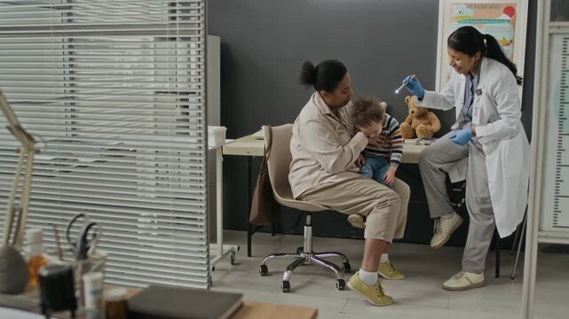Hispanic female pediatrician examining toddler sitting on biracial mothers lap in clinic. Clip is ideal for pediatric healthcare and family medicine marketing