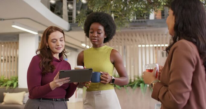 Diverse female coworkers reacting and reviewing report after tablet angling, pointing in atrium