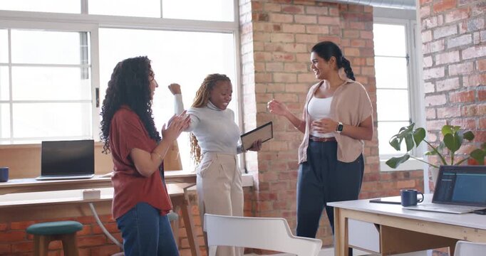 Diverse female coworkers celebrating framed certificate reveal in loft office, hugging and clapping