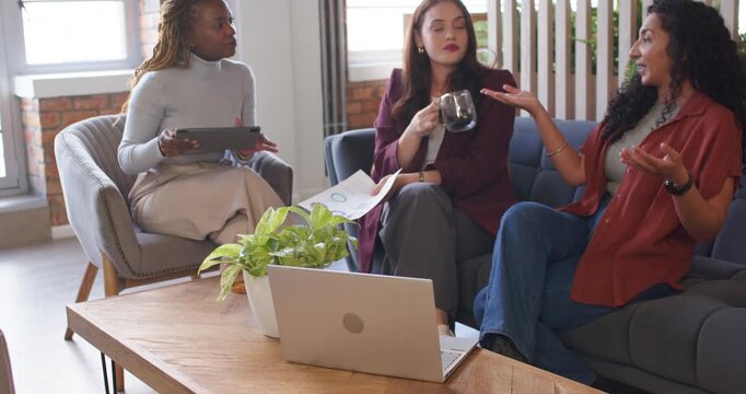 Diverse women in work clothes at lounge right explaining left pointing tablet aligning charts