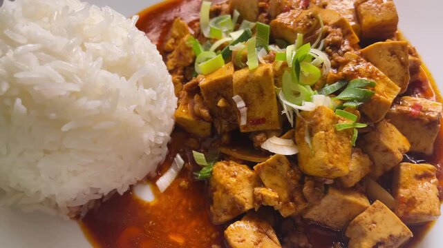 Spicy mapo tofu with steamed rice, silky tofu cubes in chili oil and savory minced sauce, sprinkled with chopped scallion on white