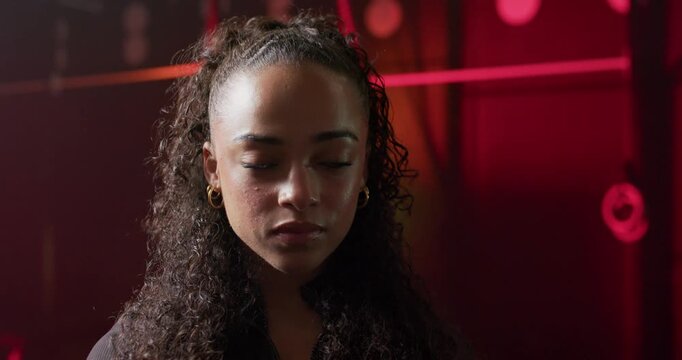 African American woman softening gaze as red panel brightening, posing in studio with gold hoops