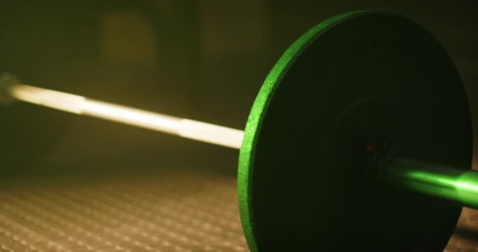 Camera is shifting, light is brightening, green plate and bar are revealing rubber floor at gym