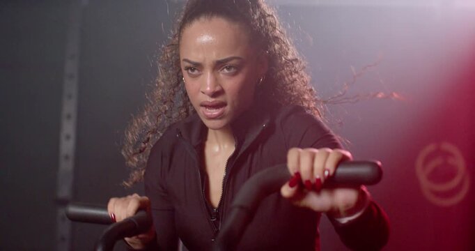African American woman beginning set at gym, gripping bike handles in zip-up top, pulling for power