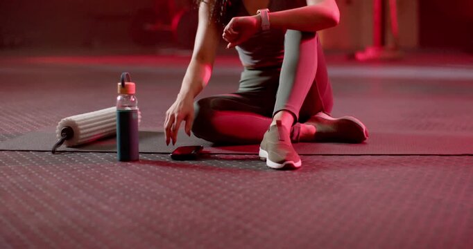 Post-workout African American woman sitting on mat by roller placing phone tapping smartwatch