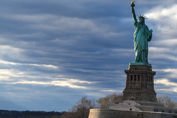 Fototapeta premium The Statue of Liberty standing proudly beneath dramatic storm clouds in New York Harbor, with expansive copy space ideal for travel, tourism, editorial design and commercial marketing projects.