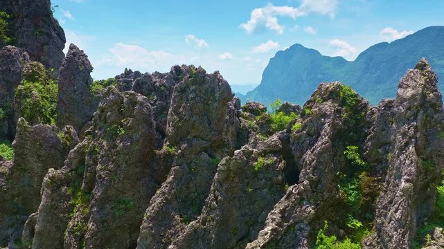 Aerial view of sharp karst rock formations covered in green vegetation, featuring dramatic mountain ridges under a blue sky in Guilin, China.
