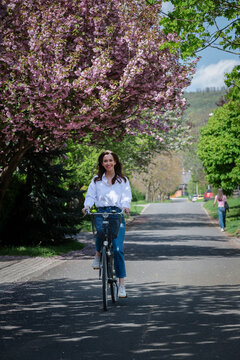 Woman riding bicycle on road lined with cherry blossoms
