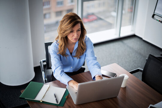 Confident middle-aged businesswoman using her laptop in a modern office