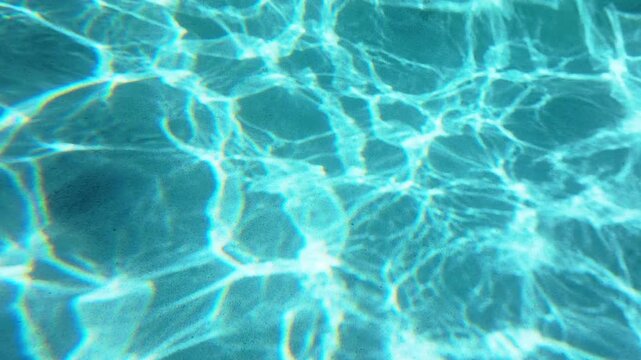 Crystal clear turquoise swimming pool water with beautiful sunlight caustic patterns dancing on the sandy bottom. Light rays create mesmerizing ripple reflections in bright blue aqua tones.