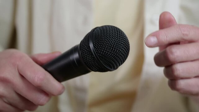Journalist holding microphone during an interview. Close-up shot of a reporter holding a professional microphone and gesticulating with their other hand, getting ready for an interview