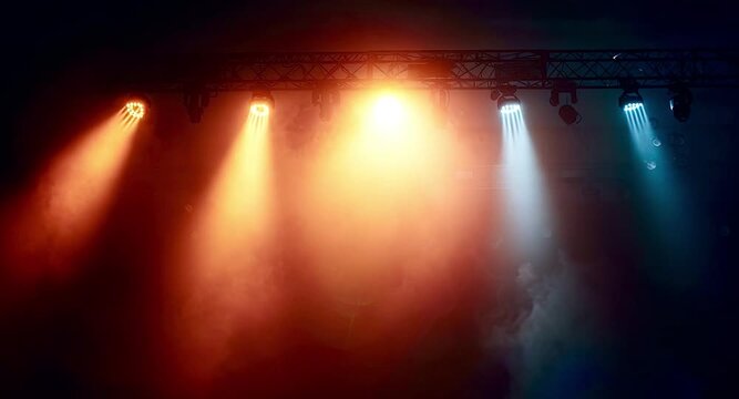 Rows of vibrant orange and blue spotlights hanging from a ceiling rig moving and projecting bright beams of light through a smoky atmosphere during a live performance in a dark venue