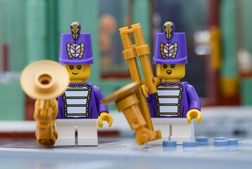 Fototapeta premium Tambov, Russian Federation - July 14, 2026 Two Lego marching band musician minifigures wearing purple uniforms and tall hats hold golden wind instruments on a city street.