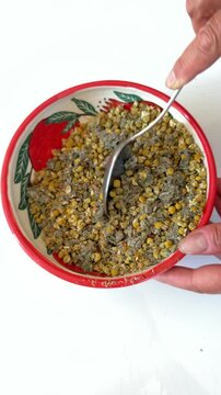 Close up of hand stirring dry medicinal herbs with a spoon in a colorful ceramic bowl.