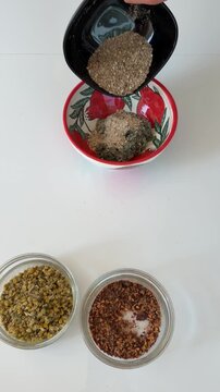 Hand pouring different types of dry healing herbs into a ceramic bowl to create a blend.