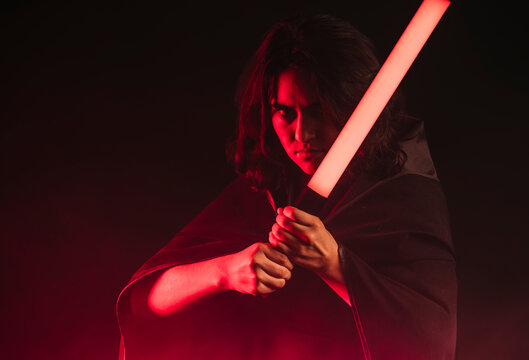 Horizontal portrait of a girl cosplaying as a Sith from the Star Wars saga, with her lightsaber in front of her.
