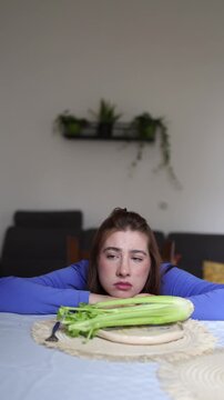 Vertical screen Young woman with anorexia sits emotionally exhausted in front of untouched celery highlighting the psychological burden of eating disorders beyond physical nutrition