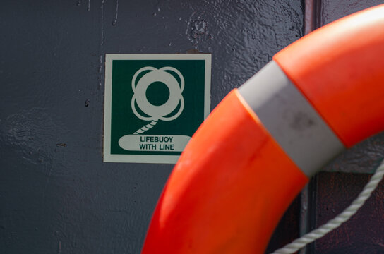 Lifebuoy mounted on board an offshore support vessel adjacent to its identification sign. The life-saving appliance is positioned for immediate deployment during a man overboard emergency.