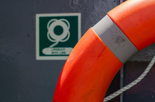 Lifebuoy mounted on board an offshore support vessel adjacent to its identification sign. The life-saving appliance is positioned for immediate deployment during a man overboard emergency.