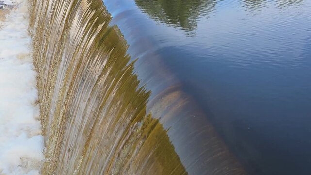Water flowing over a low-head dam into a river, showing a smooth crest transition into a rushing waterfall. video template with sound