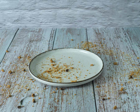 Empty ceramic plate with leftover cookie crumbs, rolled wafers, and fresh blackberries on a rustic wooden table after eating a delicious dessert