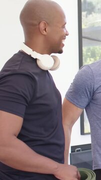 Vertical video: Smiling man holding green mat leaning into friend after smiles in studio in tees