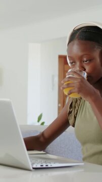 Vertical video: Sipping teen green drinking juice typing laptop at home as parent joins, copy space