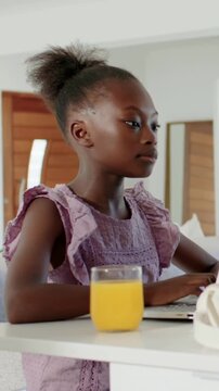 Vertical video: Reacting to laptop, kid moving while typing at home bar in purple dress and juice
