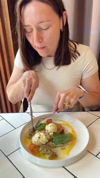 Female hands using cutlery to eat gourmet savory zucchini fritters with stracciatella and cherry tomatoes in a modern restaurant