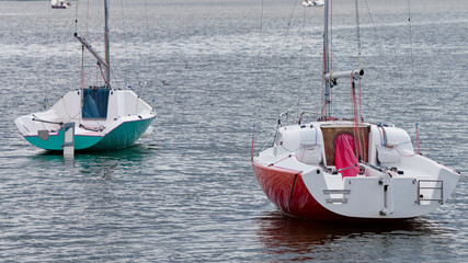 A red and a green small yacht float quietly on a tranquil lake with lowered sails. Ideal for nautical themes, maritime hobbies, and relaxing summer vacation backgrounds. Photo © slexp880