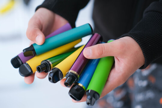 A child is holding many colorful vapes. A dangerous addiction. Vaping among teenagers.