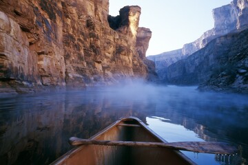Fototapeta premium Misty canyon river seen from canoe with wooden paddle at dawn