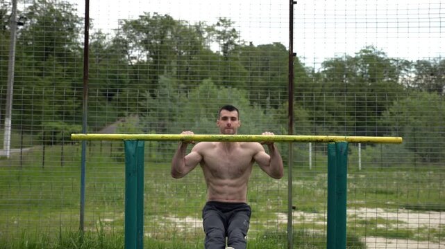 Hardy shirtless sportsman doing exercises on parallel bars at nature. Strong and muscular man working out at sports ground. Young athletic guy exercising outdoor. Concept of active healthy lifestyle