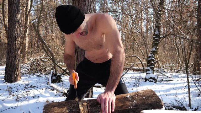 Shirtless man sawing a log in sunny winter forest. Strong guy working with saw in snowy woodland. The scene highlights human effort and outdoor activity in cold conditions. Slow motion